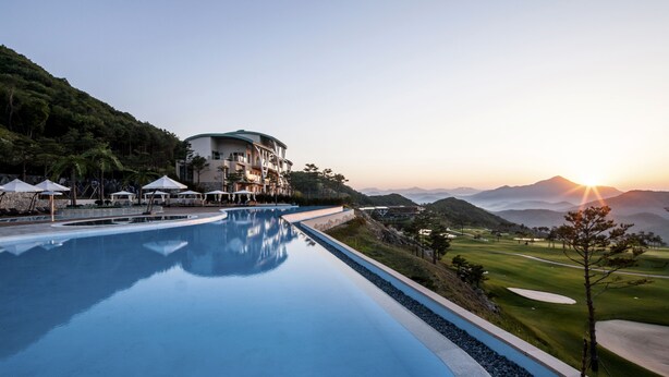 A resort with a swimming pool, a golf course, and a building with a green roof.