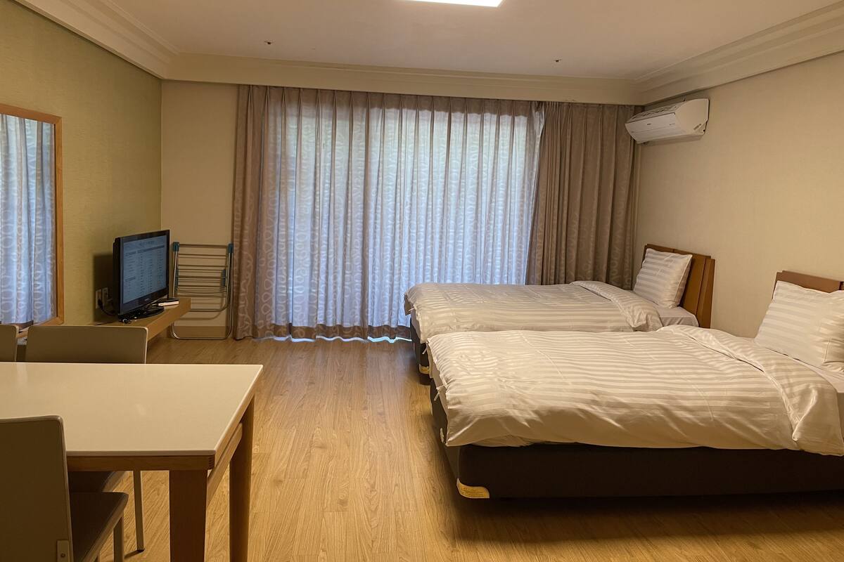 A hotel room with two beds, a desk, a television, and a window with curtains.