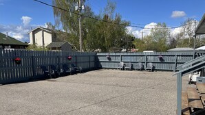 Un espacio al aire libre con piso de grava, una terraza de madera, sillas de metal y una valla.