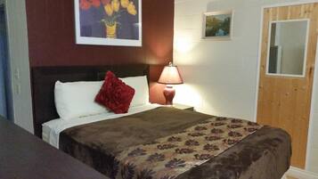 A hotel room with a bed, a nightstand with a lamp, a wooden door, and two framed pictures on the wall.