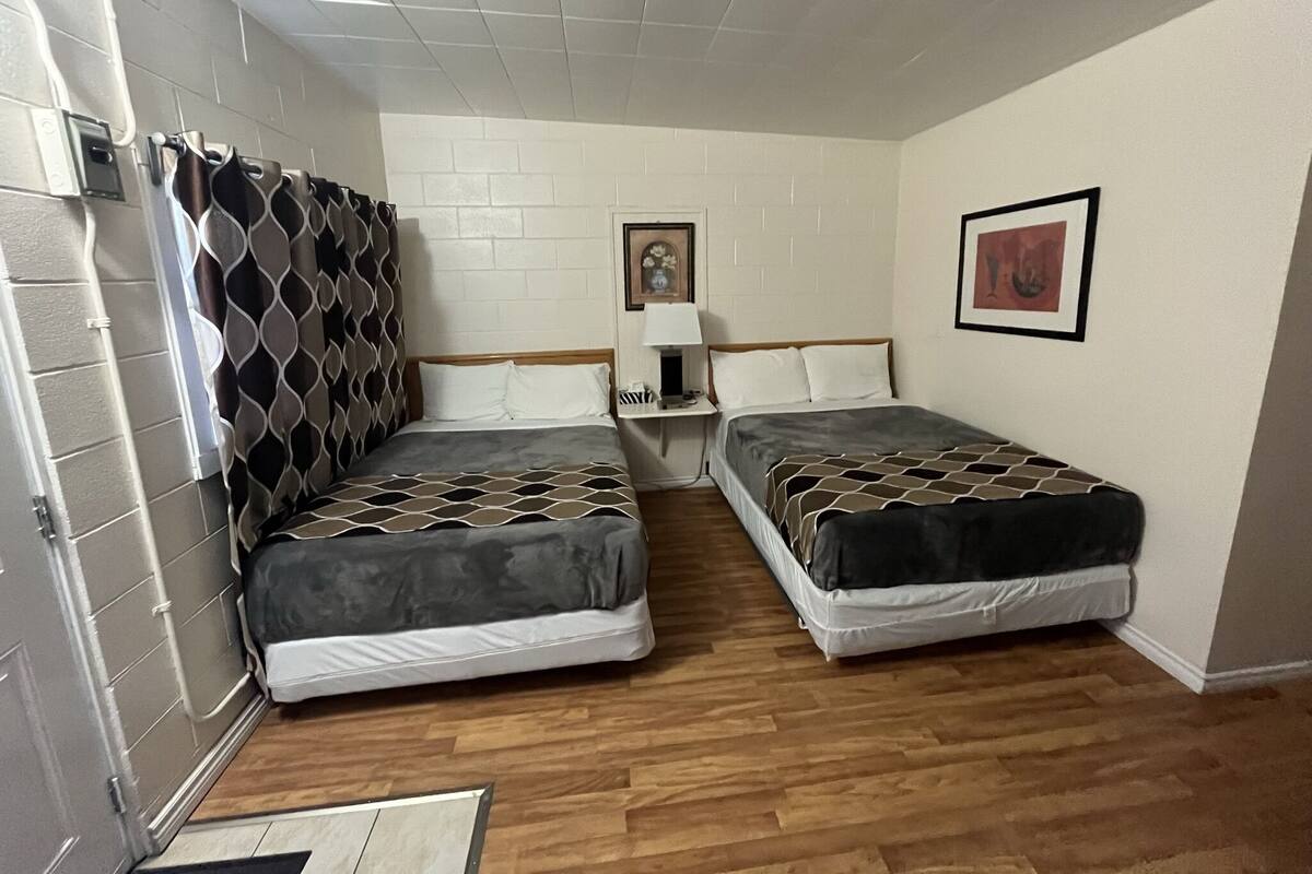 A small, clean room with two beds, a nightstand, a lamp, and a picture on the wall.