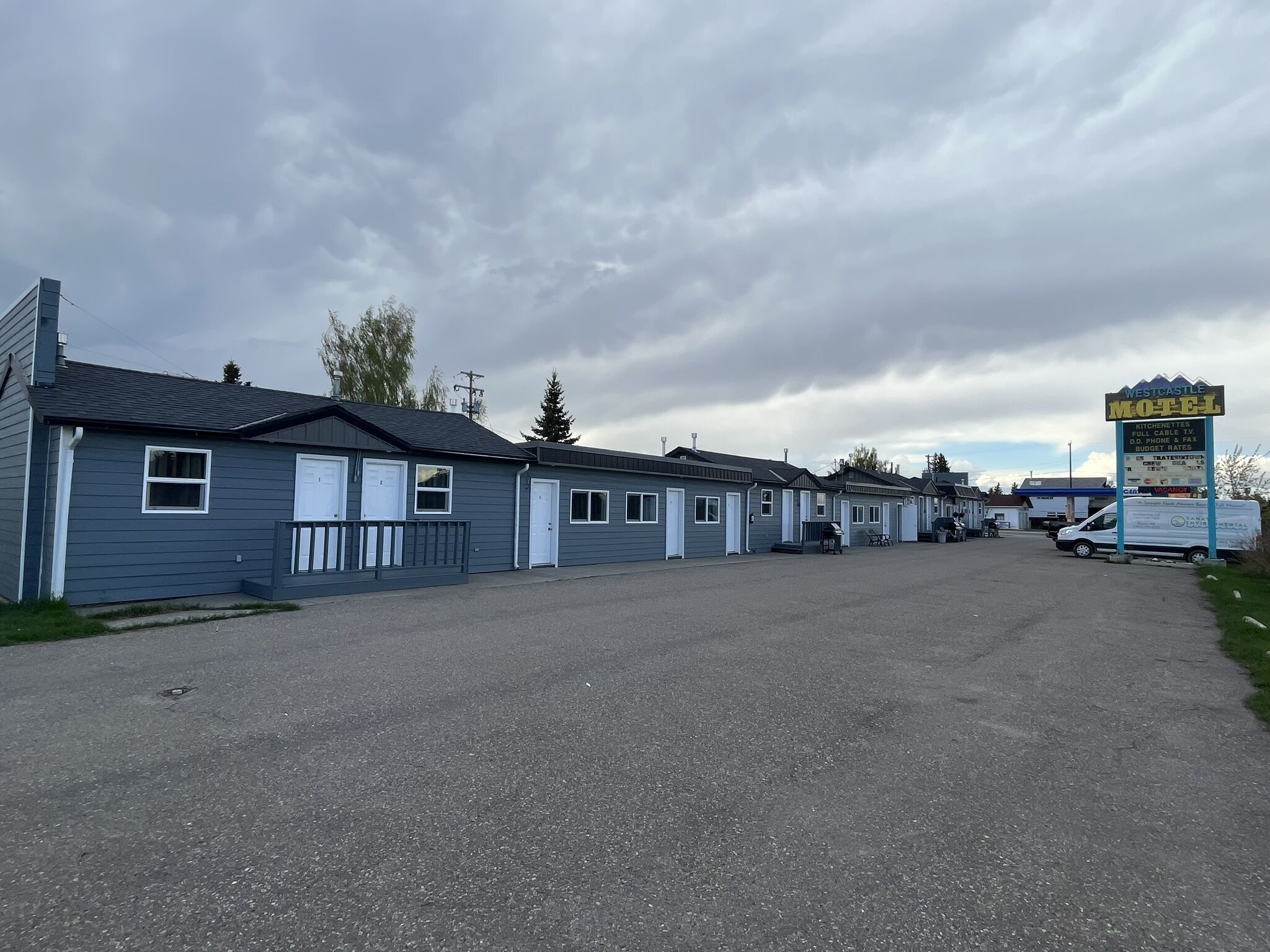 A row of single-story motels with a gravel driveway, a signboard for the VESTCASTLE MOTEL, and a gas station in the background.
