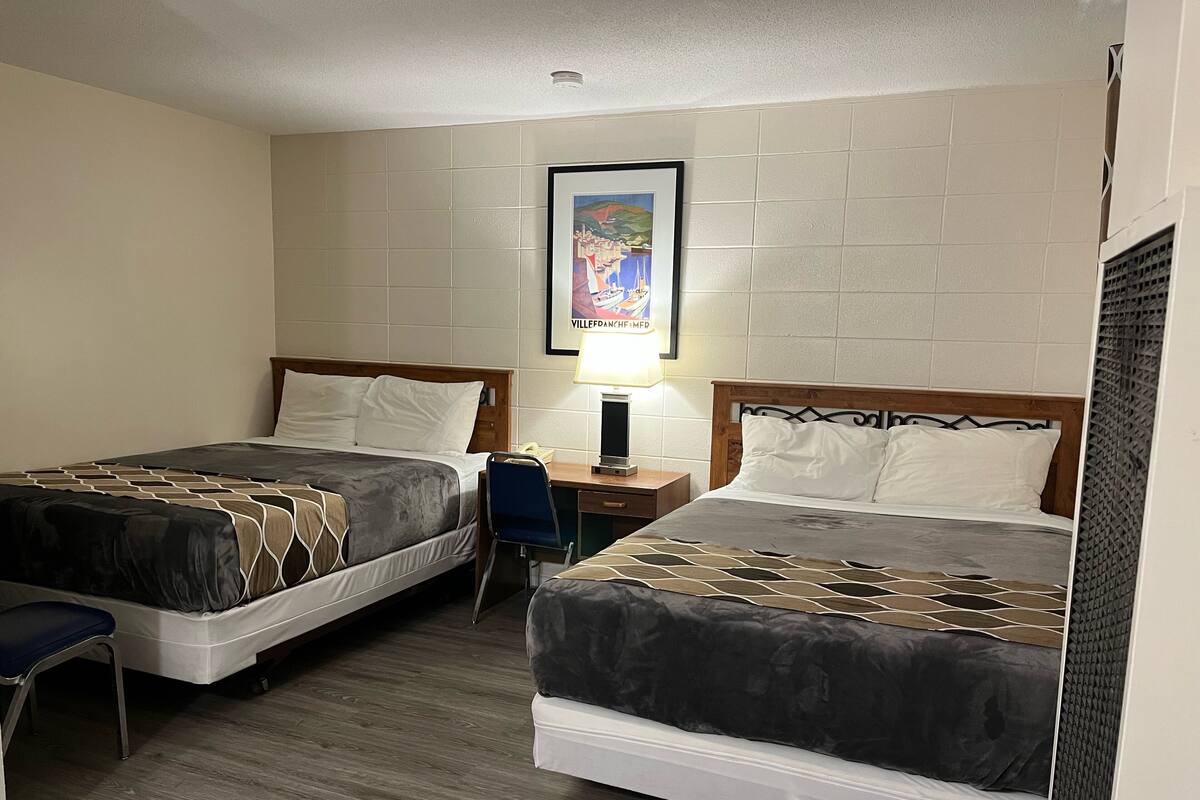 A hotel room with two beds, a desk, a chair, and a framed picture on the wall.
