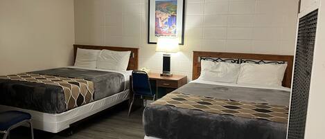 A hotel room with two beds, a desk, a chair, and a framed picture on the wall.