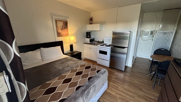 Una habitación de hotel compacta con una cama, una kitchenette pequeña, un comedor y un baño.