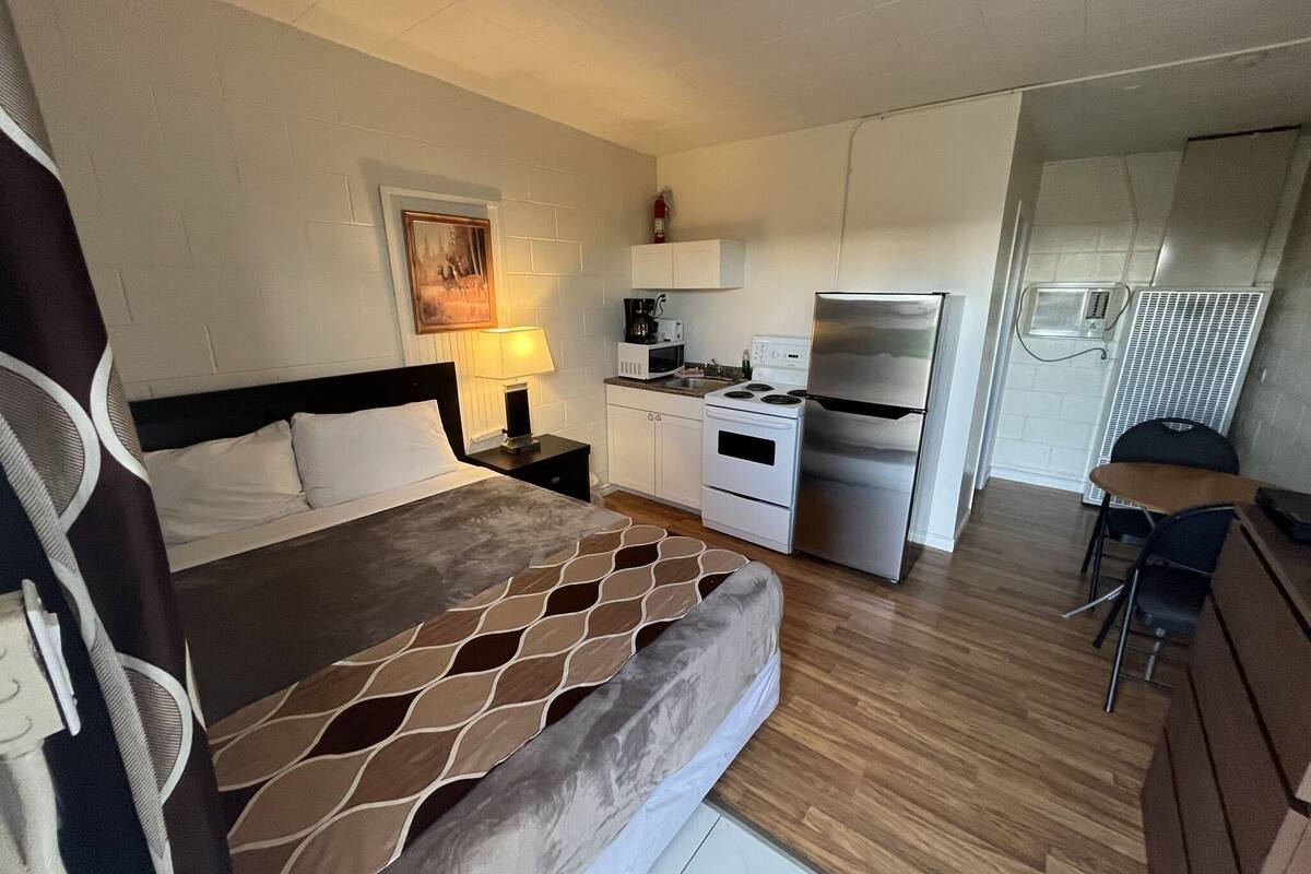 A compact hotel room with a bed, a small kitchenette, a dining area, and a bathroom.