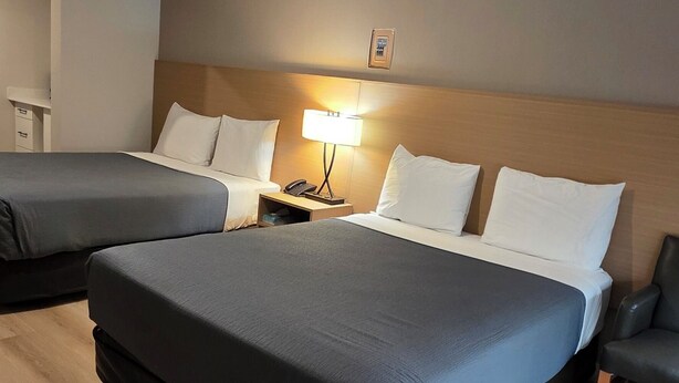 A hotel room with two beds, a nightstand, a lamp, and a wooden floor. - Parkway Motel & European Lodges (Pincher Creek)