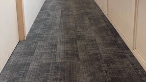Un largo pasillo con pisos alfombrados, ventanas amplias y puertas a ambos lados.
