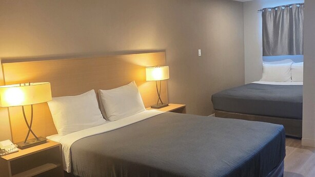 Un dormitorio con una cama, lámparas de noche, una silla, una mesita de noche y un ventanal con cortinas.