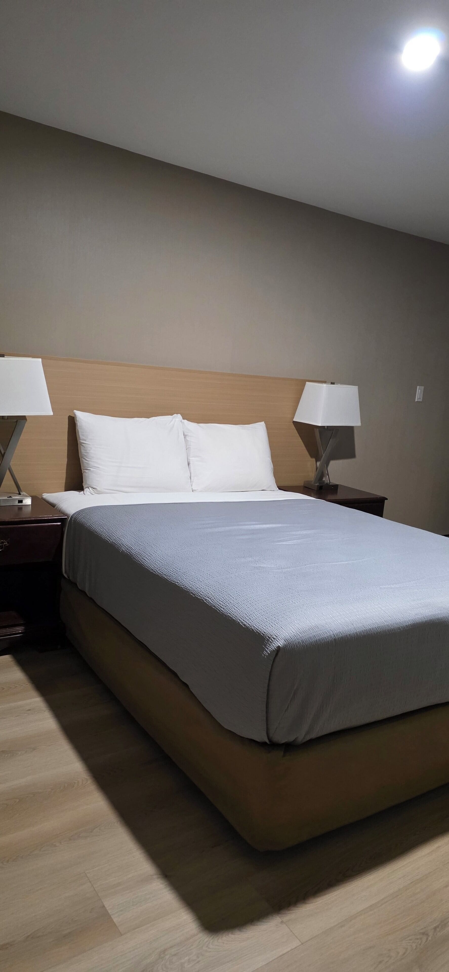 Una habitación de hotel con una cama, dos mesitas de noche y una mesita auxiliar.