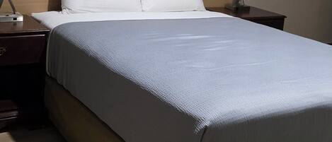 Una habitación de hotel con una cama, dos mesitas de noche y una mesita auxiliar.