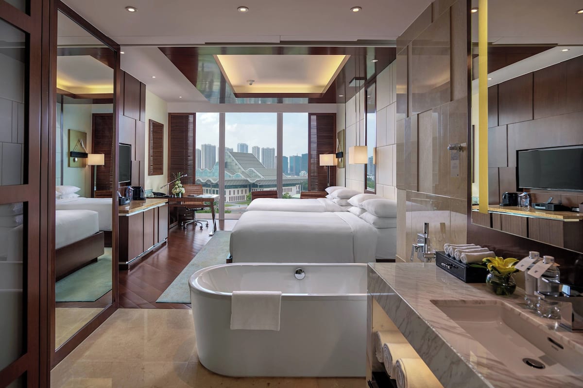 Quarto de hotel moderno com uma banheira grande, duas camas, uma TV e vista para a cidade.