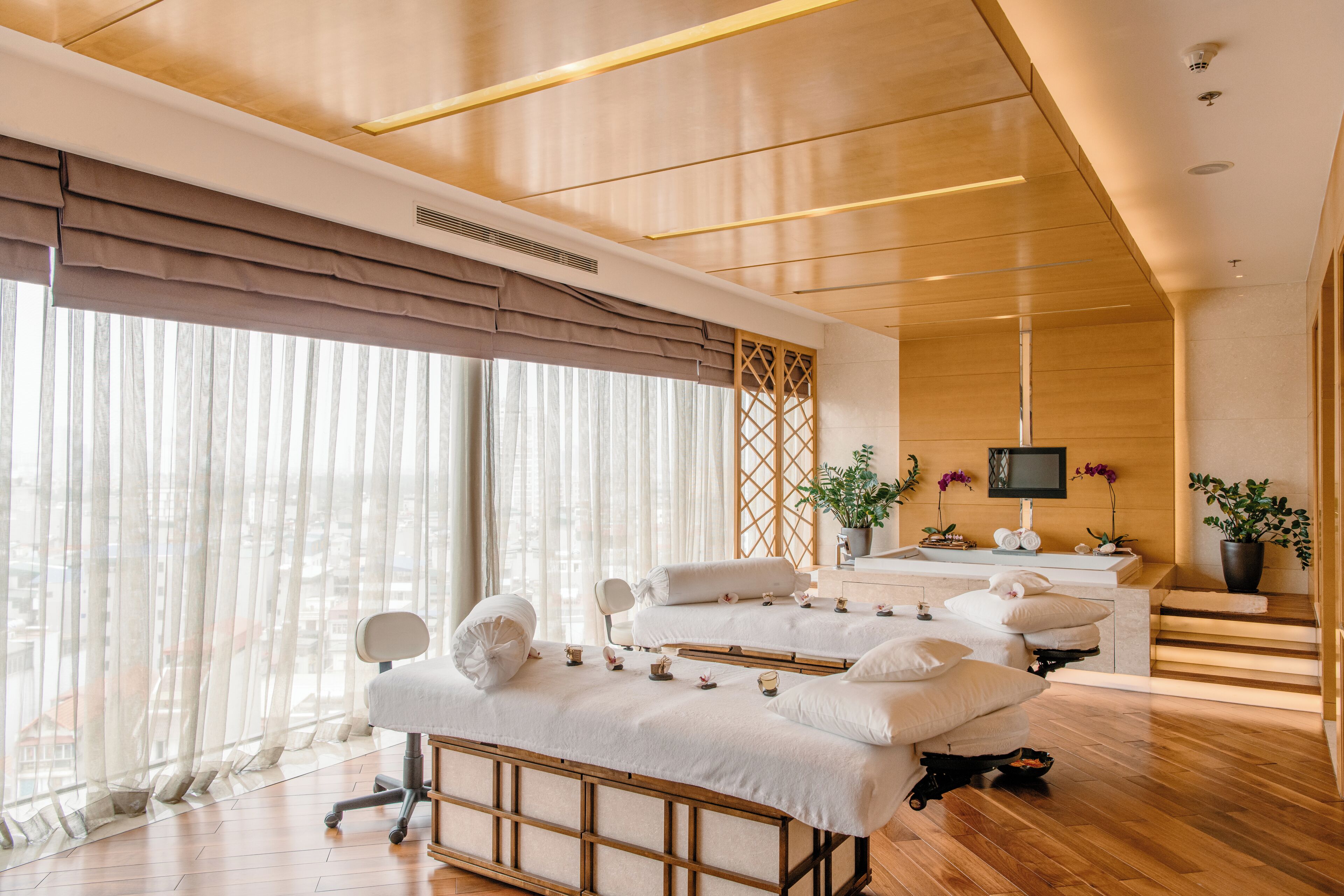 A modern spa room with a massage table, a TV, and a potted plant.