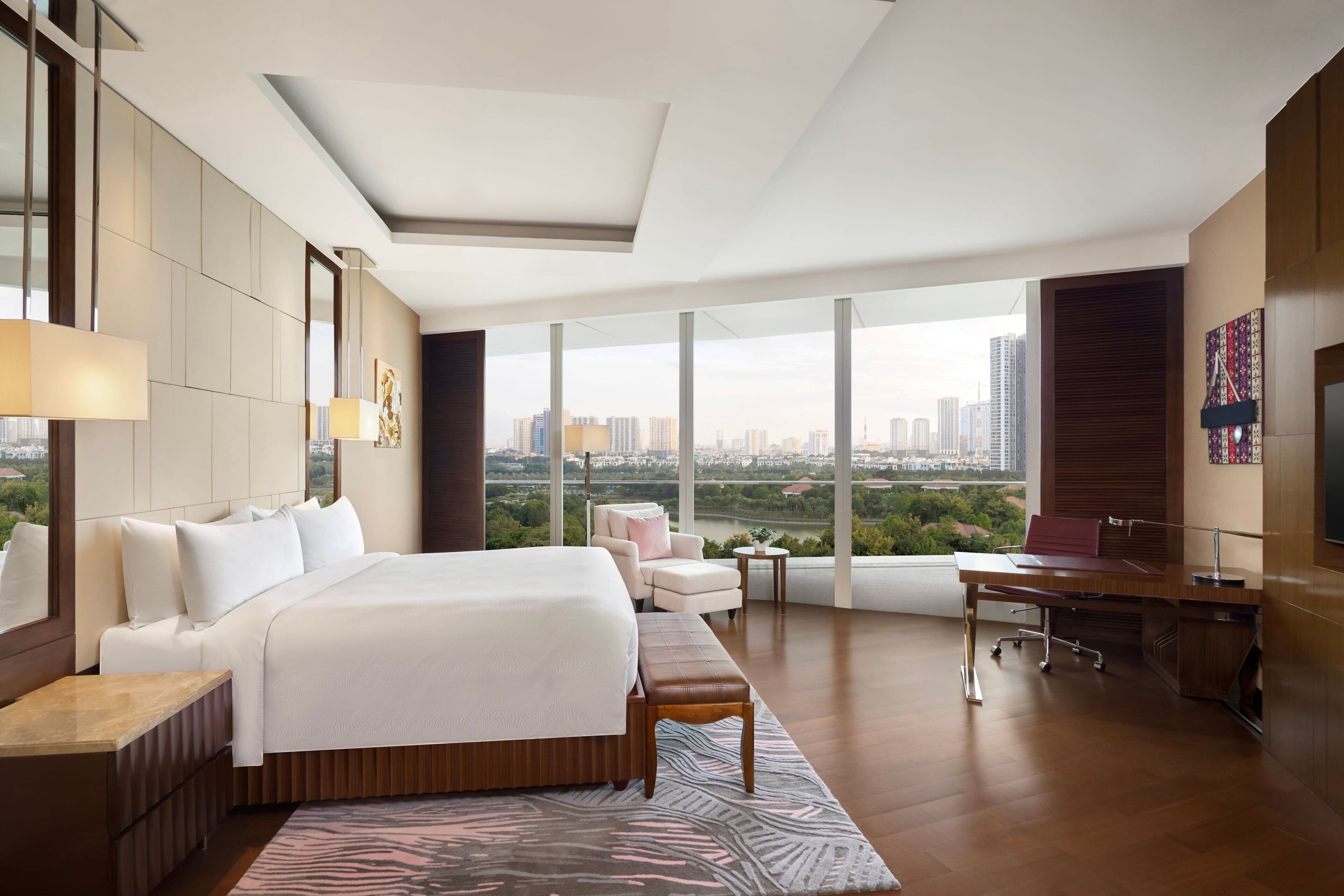 A modern hotel room with a large bed, a desk, and a view of the cityscape.