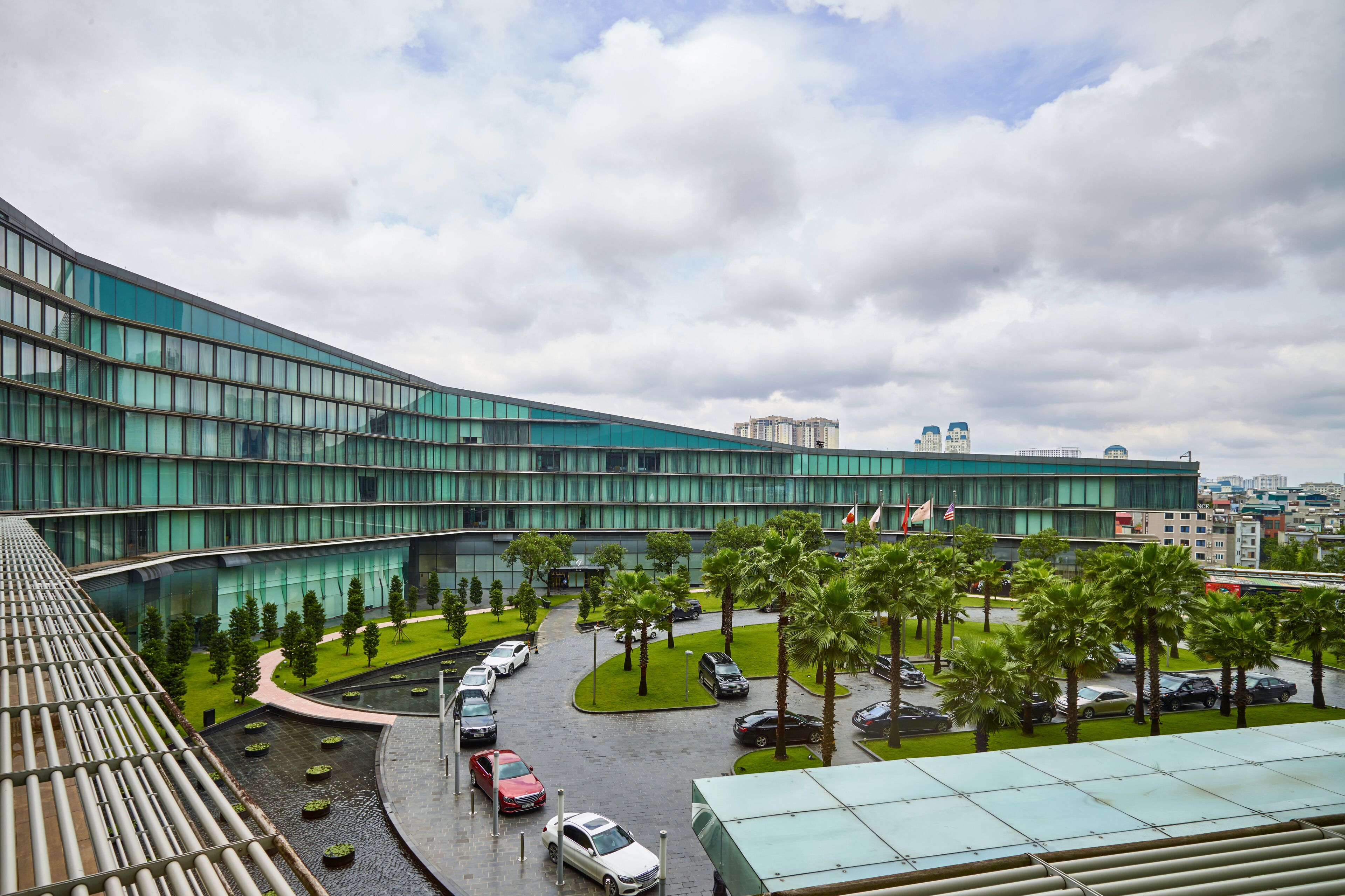 Een modern gebouw met een gebogen glazen gevel, een parkeerplaats met auto's en palmbomen.