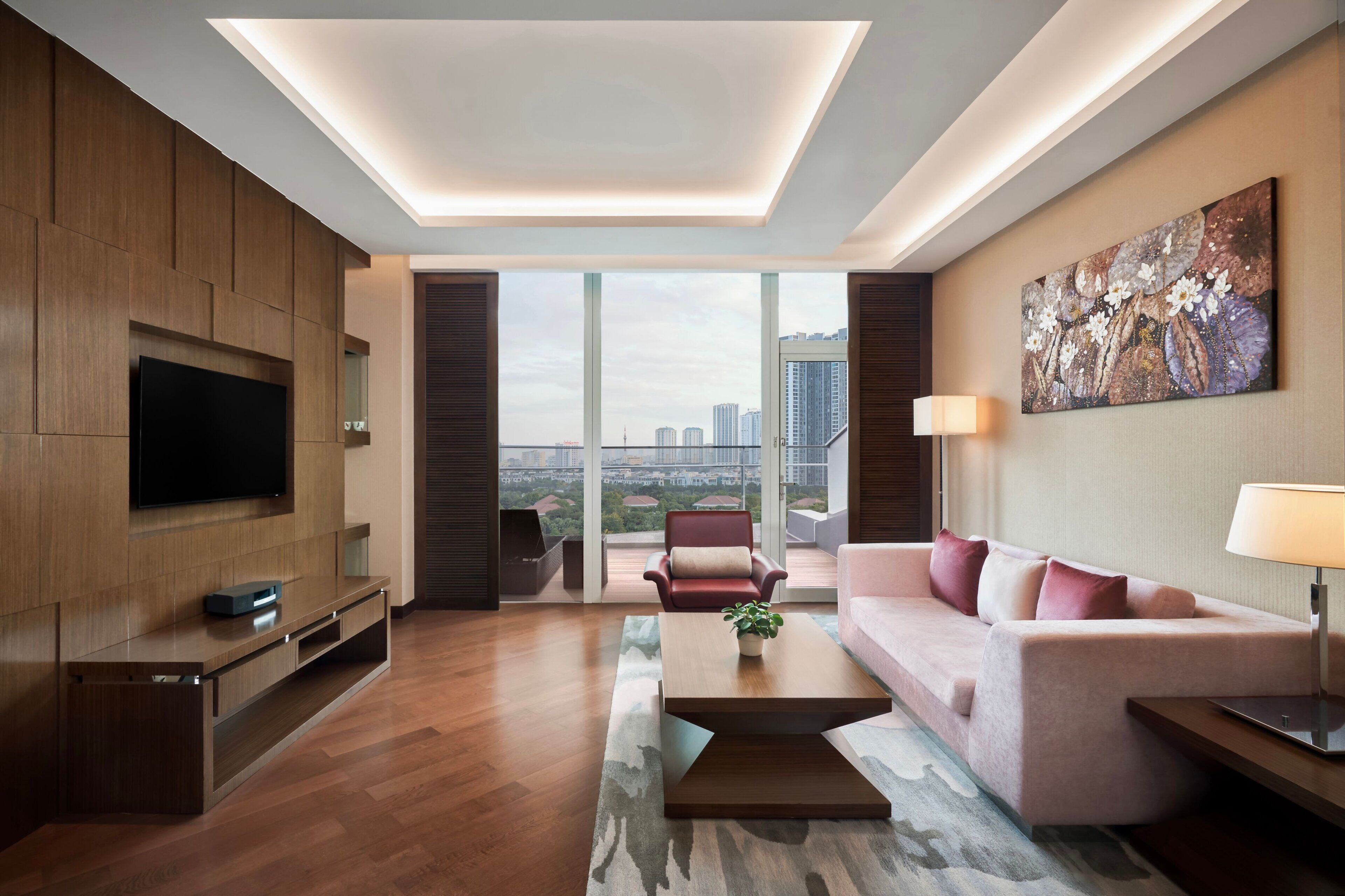A modern living room with a flat-screen TV, a sofa, a coffee table, and a city view through large windows.