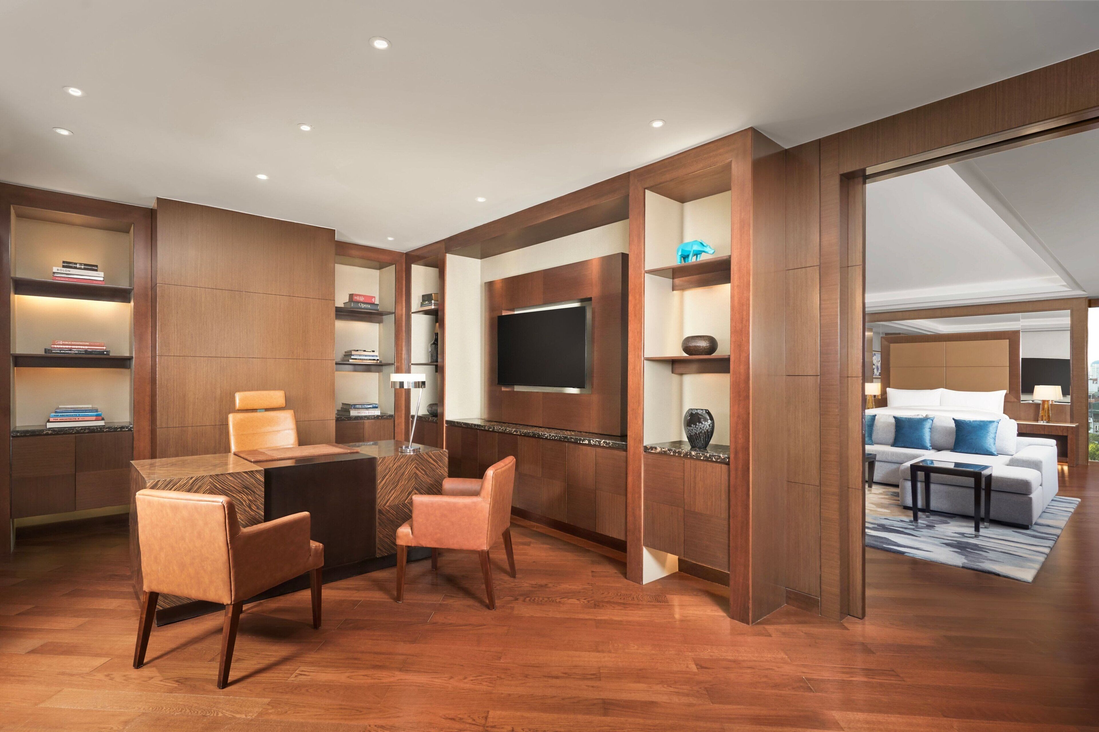 Een moderne hotelkamer met een houten vloer, een zithoek met tafel en stoelen, een flatscreen televisie aan de muur en een lounge met een bank en fauteuils.