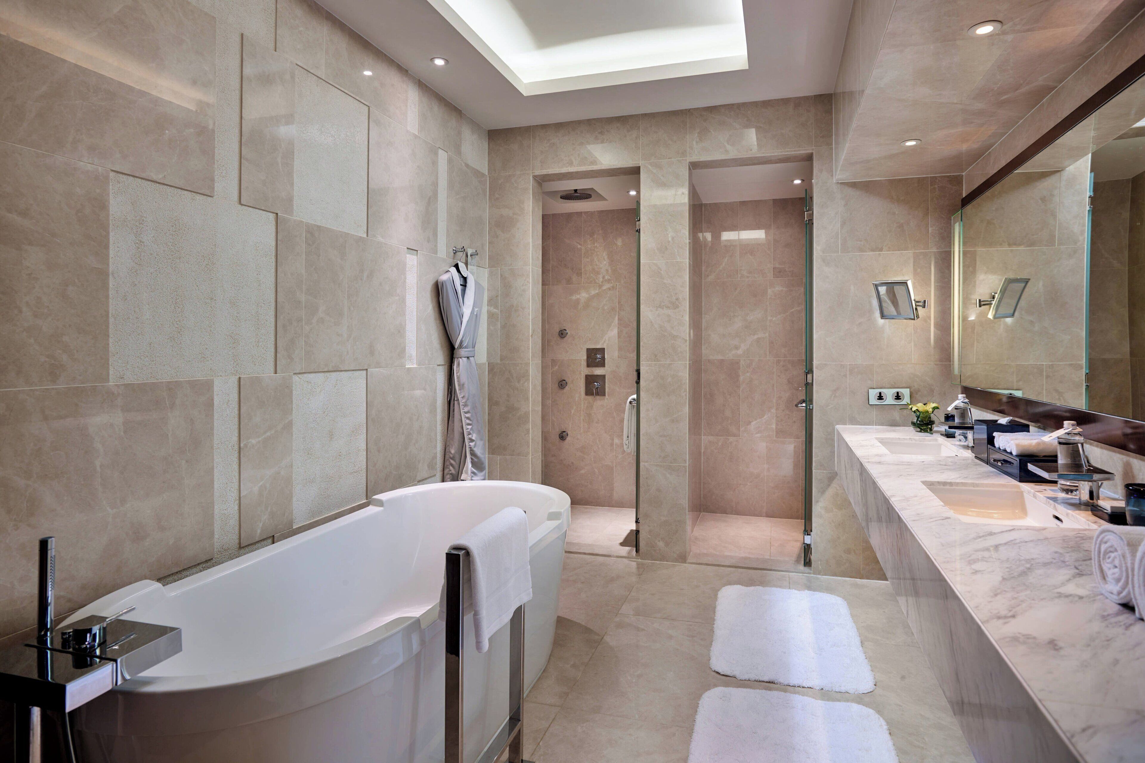 Un baño moderno con una bañera independiente, ducha a ras de suelo y un mueble de tocador amplio con espejo.