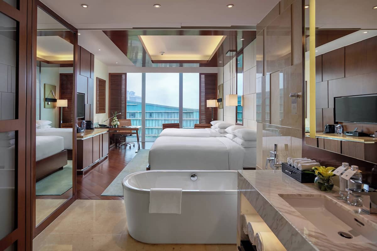 Quarto de hotel moderno com uma banheira grande, uma cama, uma escrivaninha e vista para a cidade.