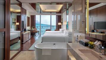 A modern hotel room with a large bathtub, a bed, a desk, and a view of the city.