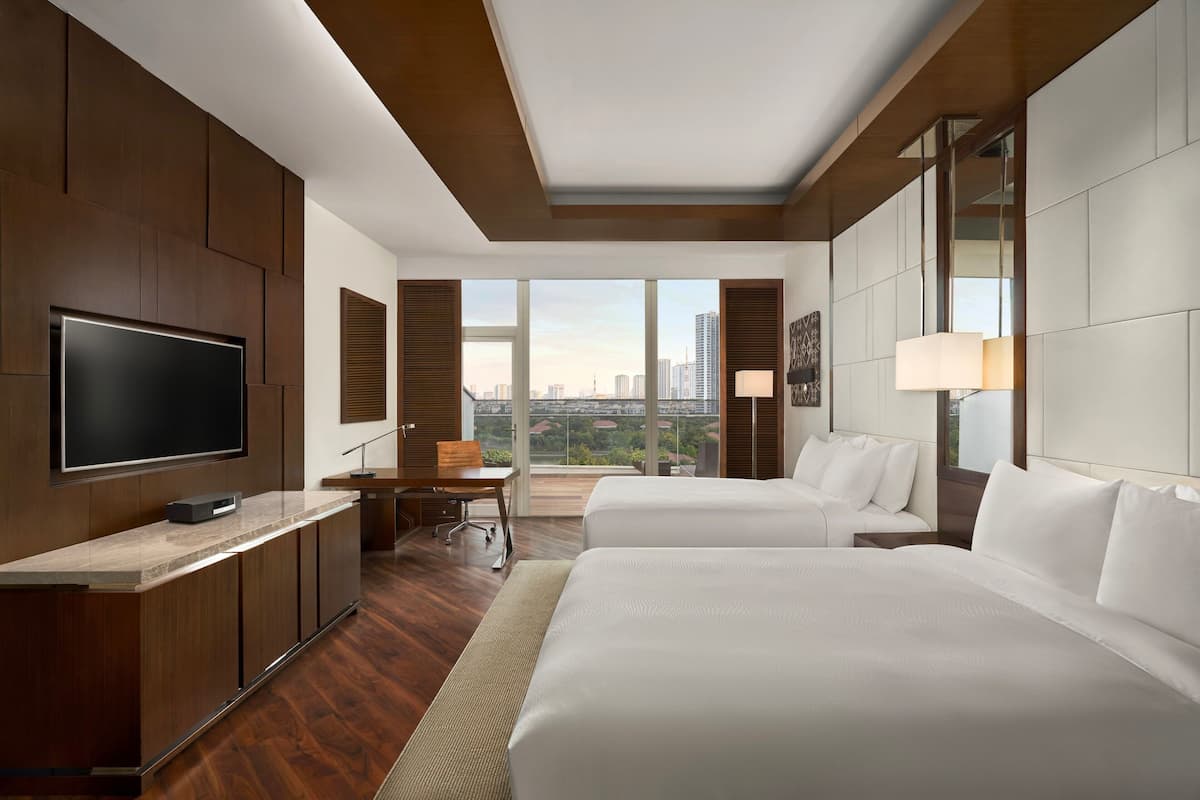 Quarto de hotel moderno com uma cama grande, uma escrivaninha, uma televisão e vista para a cidade.