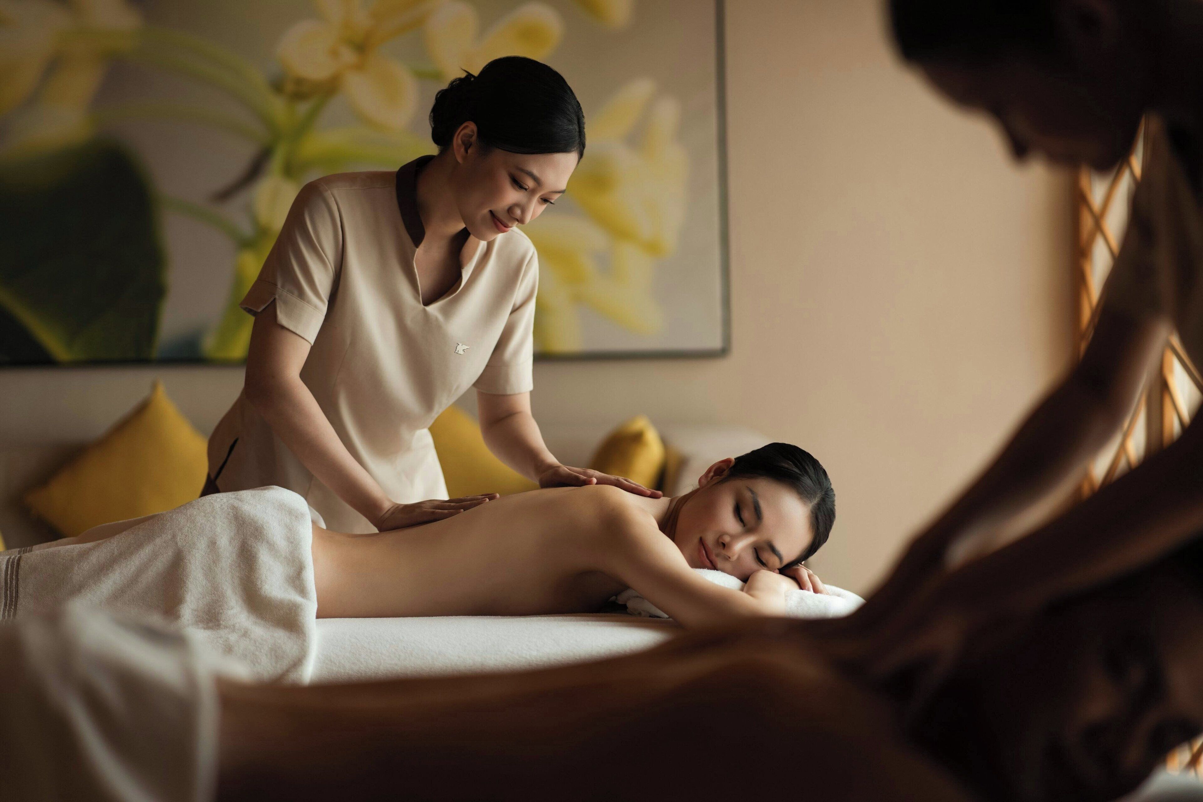 A massage therapy session in a room with a bed, a massage table, and a yellow pillow.