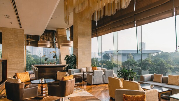 A spacious lounge area with multiple seating options, a central coffee table, and large windows offering a view of the cityscape. - JW Marriott Hotel Hanoi (Hanoi)