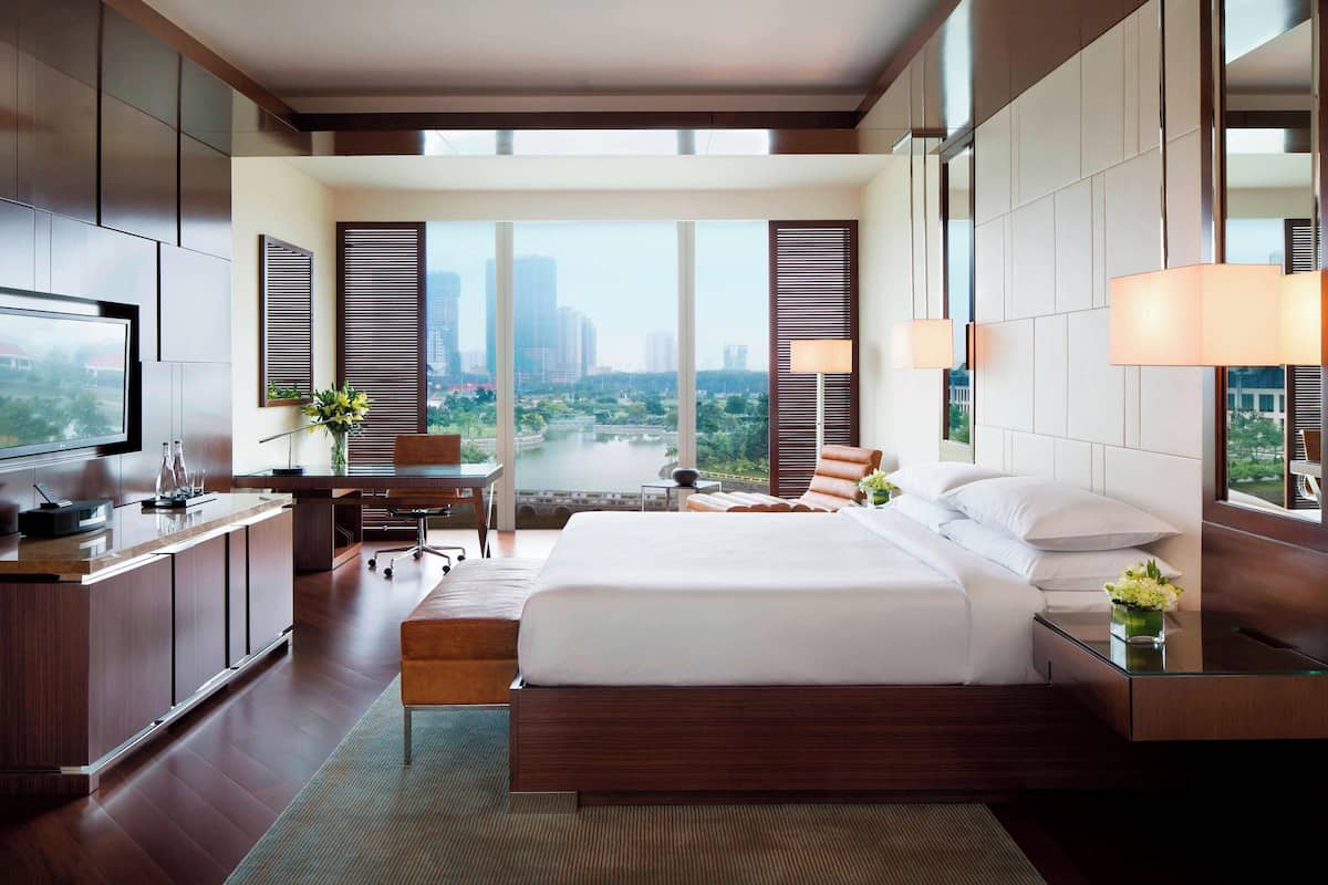 Quarto de hotel moderno com uma cama grande, uma mesa de escritório, uma televisão e vista para a cidade.