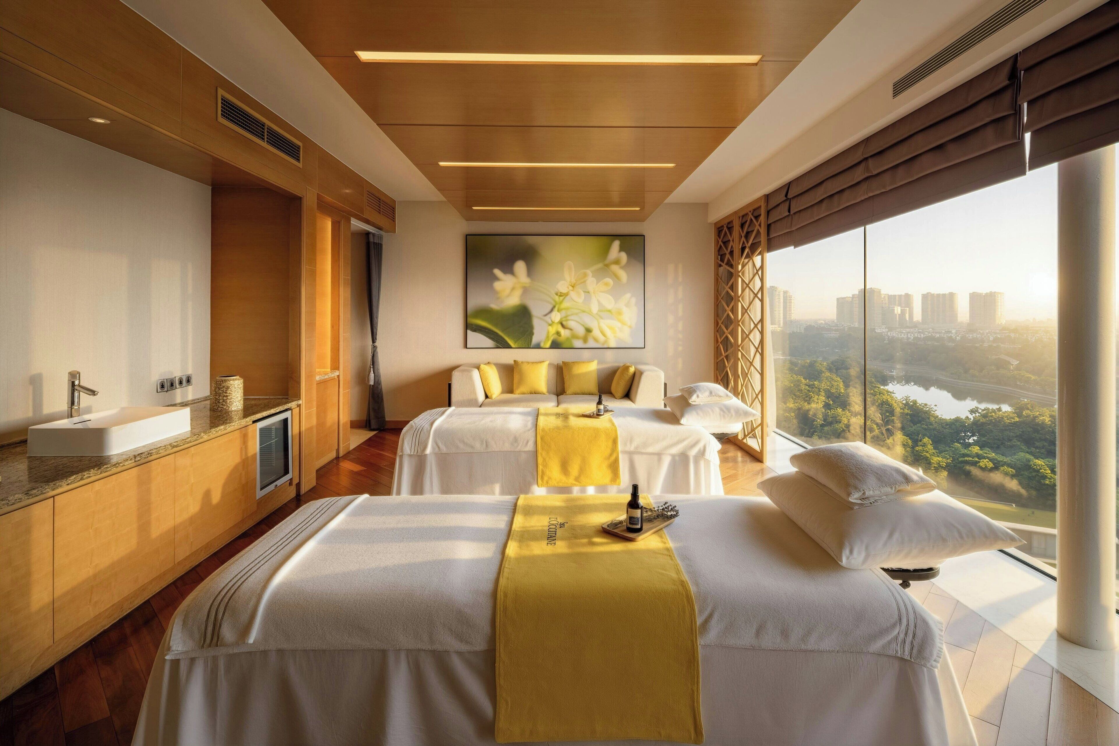 Une chambre d’hôtel avec une grande fenêtre, un lit avec une serviette jaune, une table de chevet et une vue sur le paysage urbain.