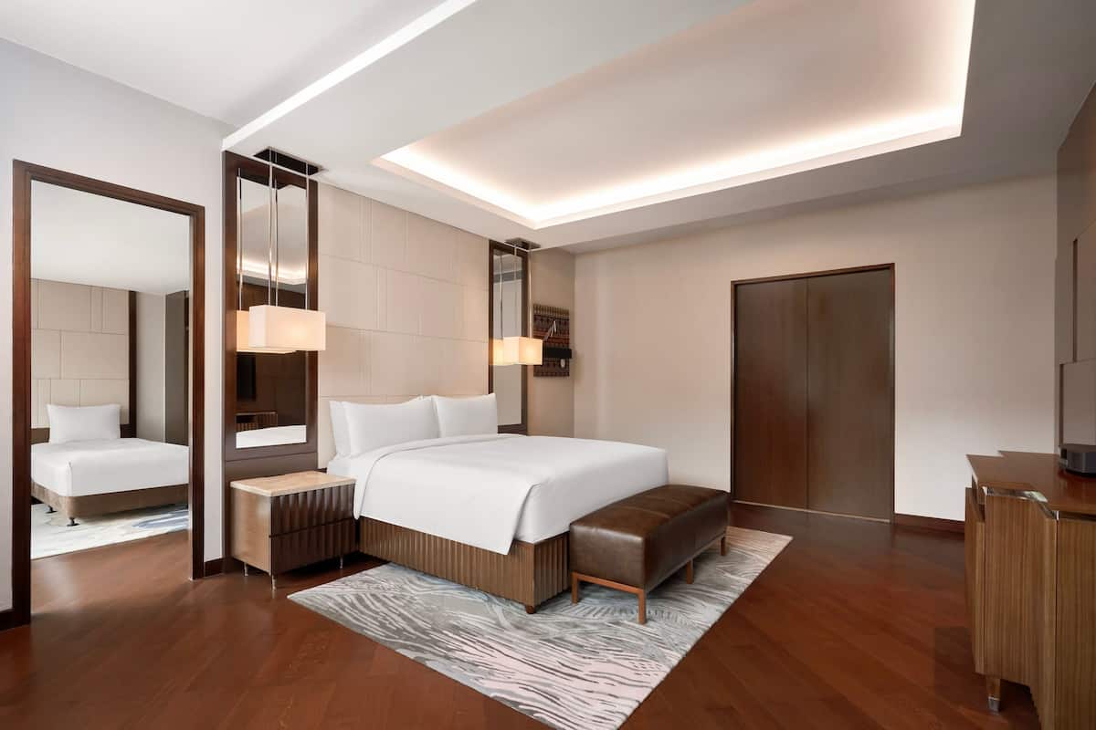Quarto de hotel moderno com uma cama grande, um banco de madeira, uma escrivaninha e um guarda-roupa.