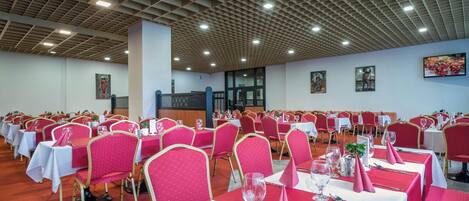 Uma sala de banquetes com fileiras de mesas e cadeiras, cada conjunto com toalhas brancas e guardanapos vermelhos.