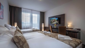 Une chambre d’hôtel avec deux lits, un bureau, une chaise, une télévision et une fenêtre avec des rideaux.