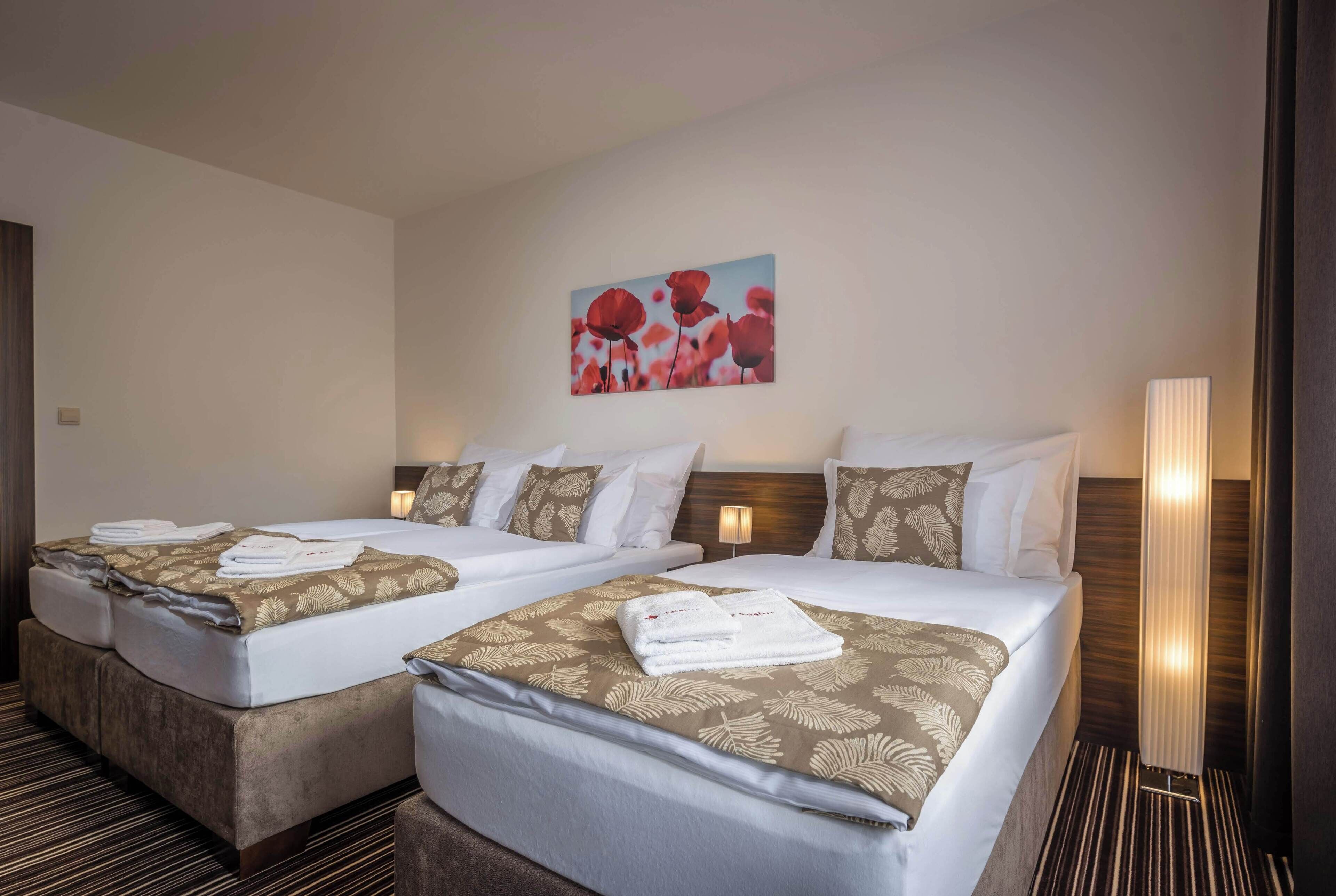 A hotel room with two beds, each with a patterned bedspread and pillows, a wall-mounted artwork, and a bedside lamp.