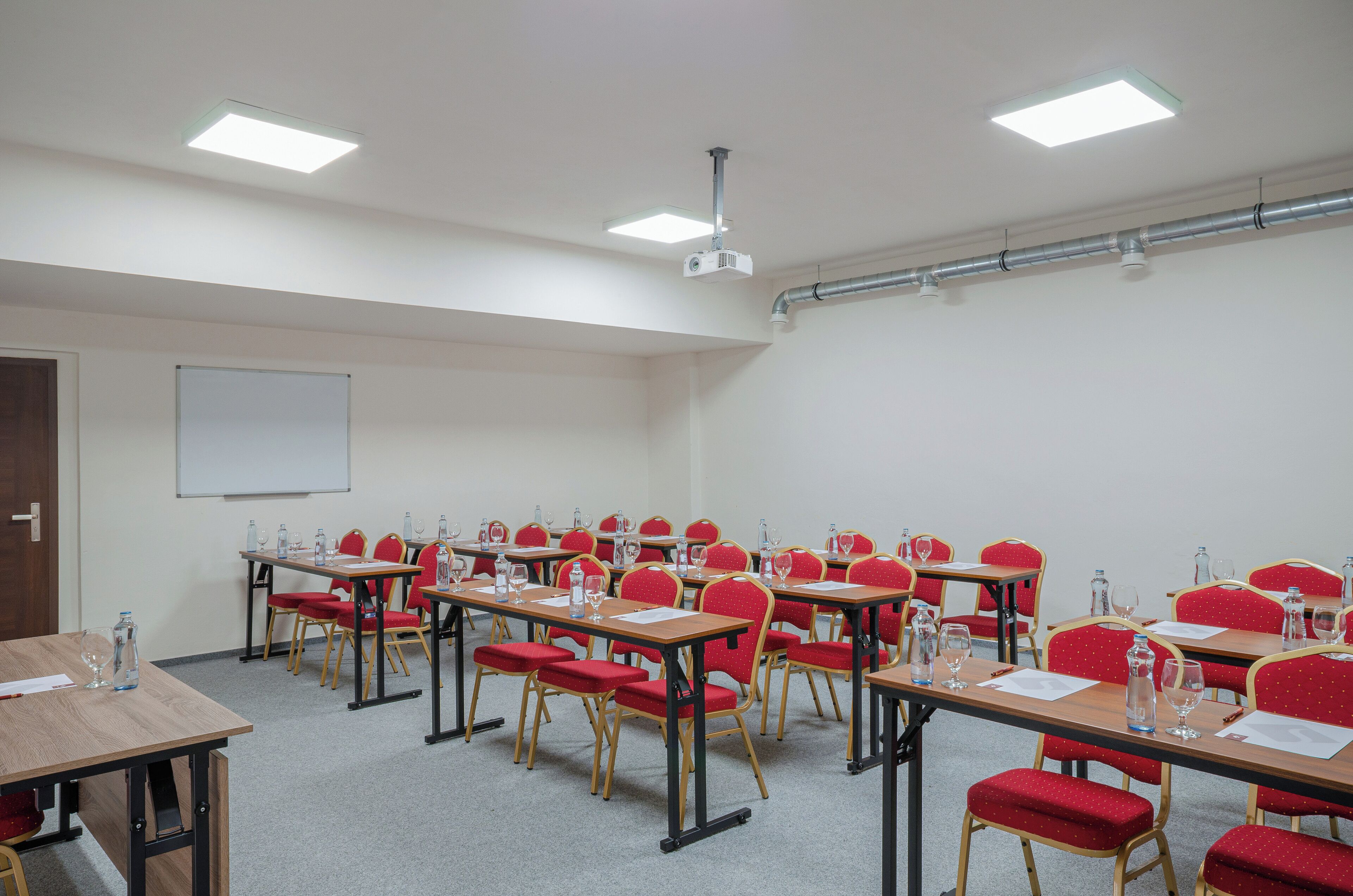 Un salón de conferencias con varias mesas y sillas rojas, equipado con botellas de agua y vasos.
