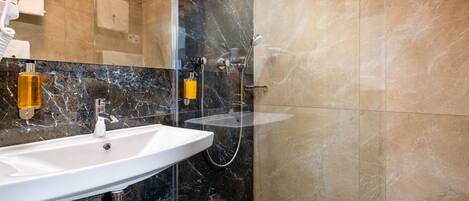 Un baño moderno con un lavamanos blanco, una ducha con cerramiento de vidrio y paredes de mármol.