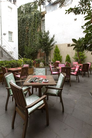 An outdoor patio with wooden tables and chairs, surrounded by greenery and a white building. - Premist Hotels Sultanahmet (Istanbul)