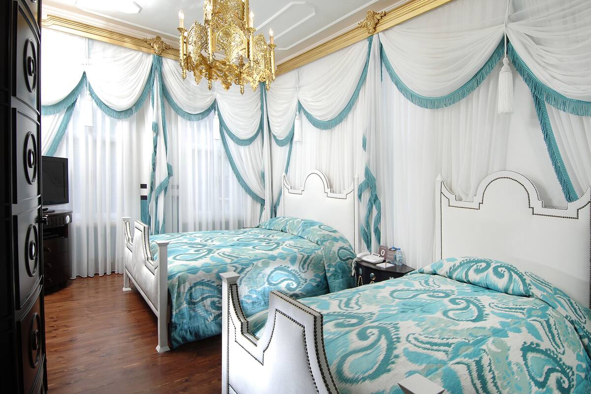 A bedroom with two beds, white drapes, a chandelier, and a television.