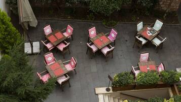 Un patio al aire libre con varias mesas y sillas, rodeado de follaje y un muro de ladrillo.