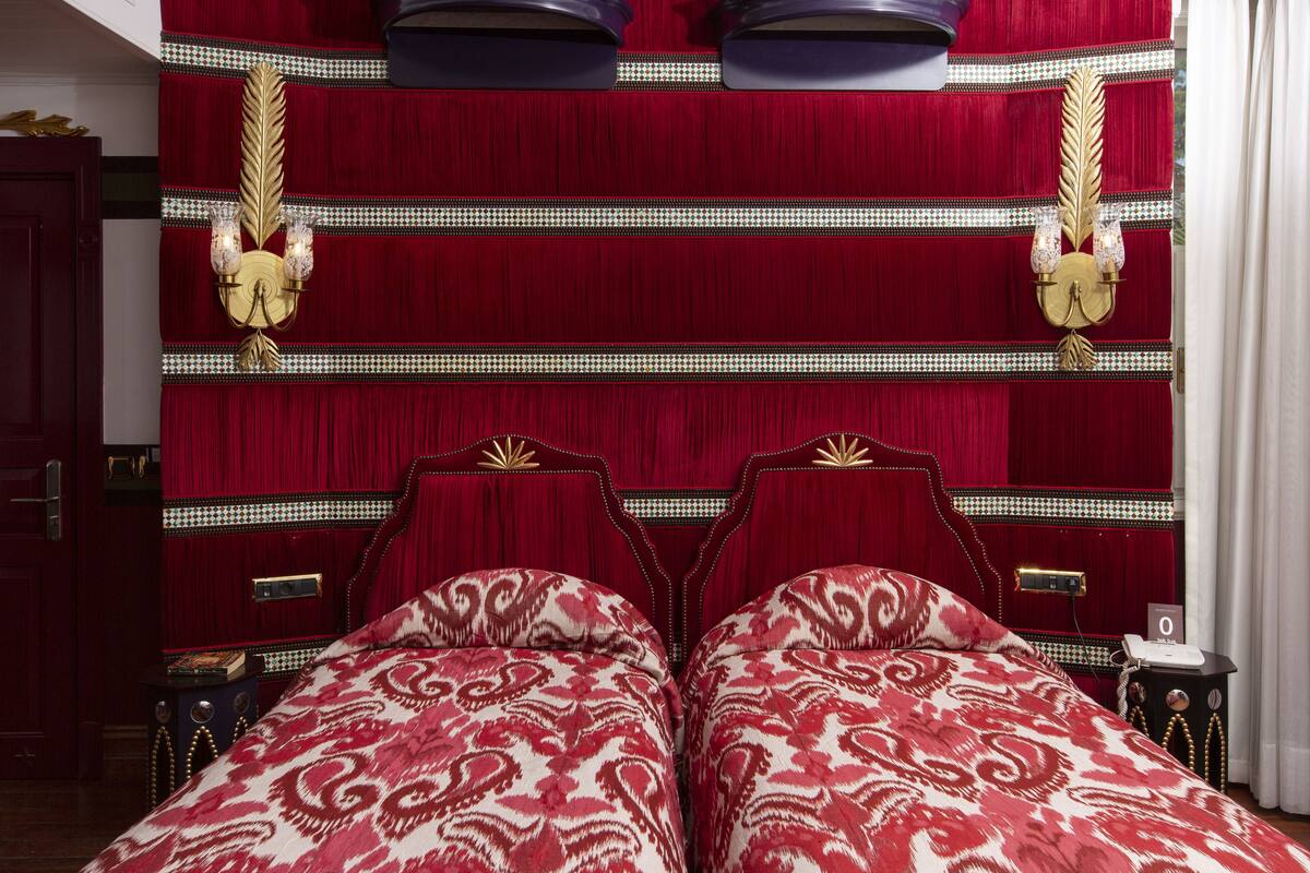 A room with a large bed, two bedside tables, a nightstand, and a red curtain.