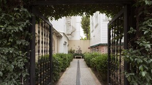 Un vialetto stretto delimitato da cancelli in ferro battuto nero, che conduce a una statua in un cortile circondato da edifici bianchi.