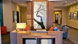 Un hall con mostrador de recepción, zona de estar y una gran obra de arte abstracto en la pared.