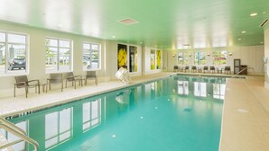 Una amplia piscina interior con ventanas transparentes, sillas y suelo de baldosas.