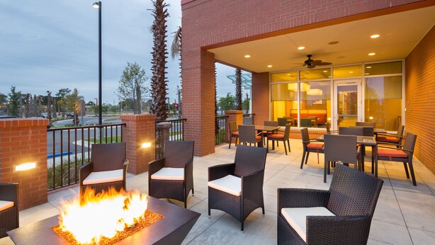 Un patio al aire libre con mobiliario de mimbre, una chimenea y una puerta de cristal que da a un espacio interior.