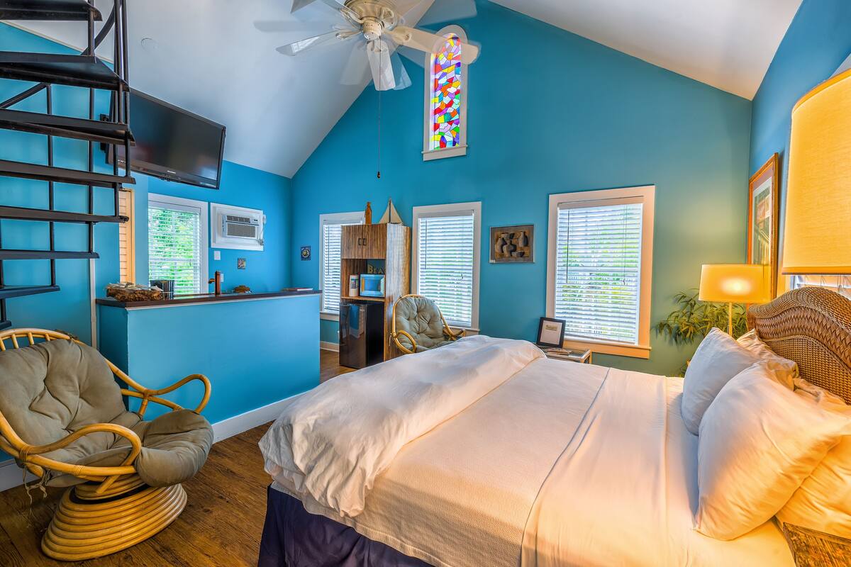 A bedroom with a bed, a chair, a desk, a TV, and a ceiling fan.