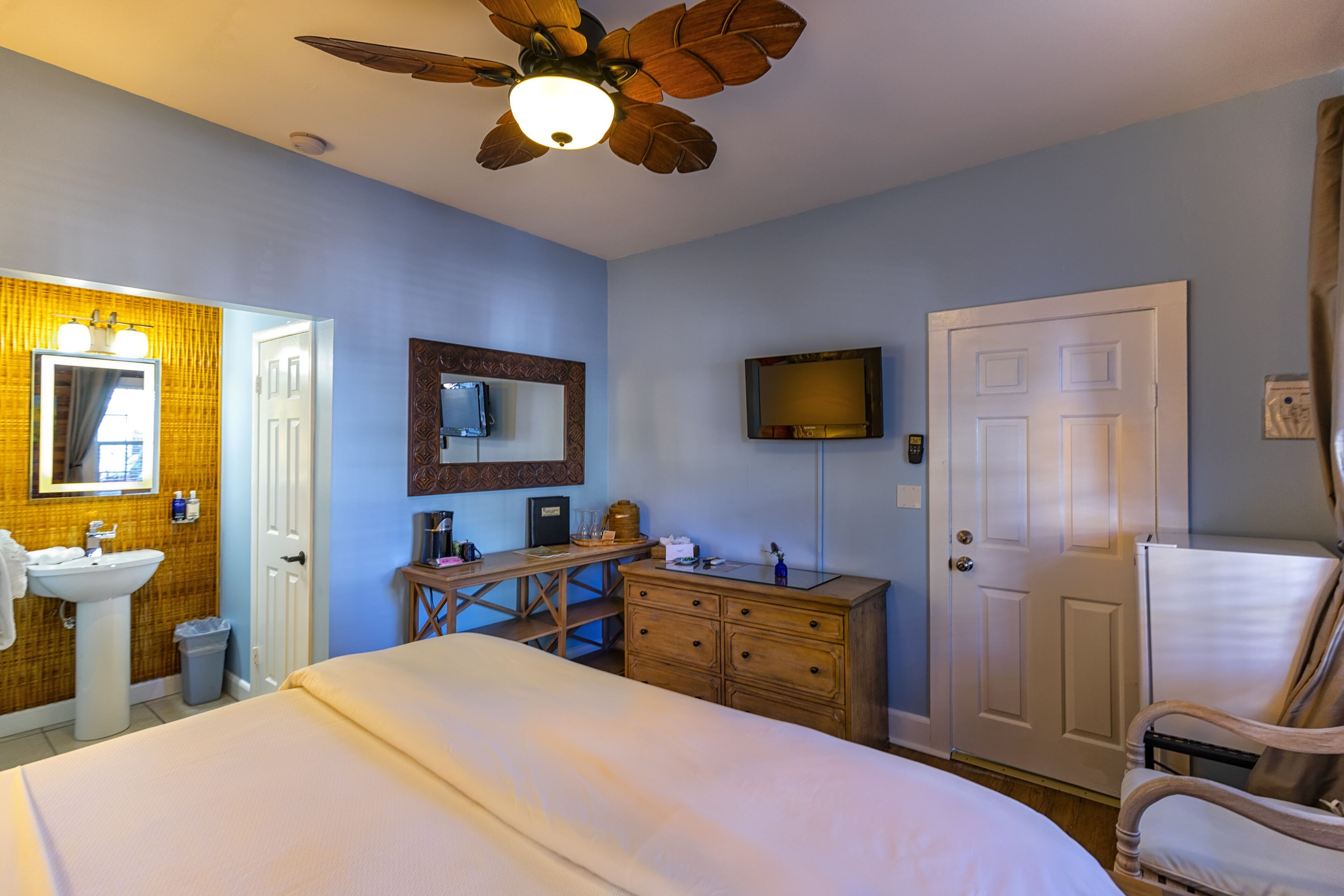 Une chambre d’hôtel équipée d’un lit, d’un bureau, d’une commode, d’une télévision et d’un ventilateur de plafond.