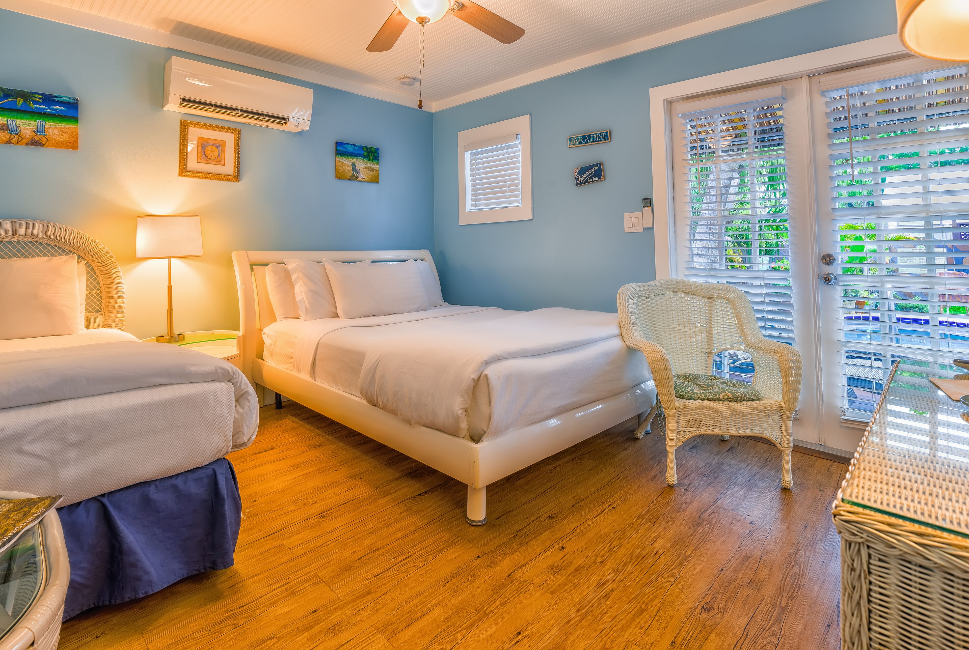 Une chambre avec deux lits, une chaise en osier et une fenêtre avec des stores.