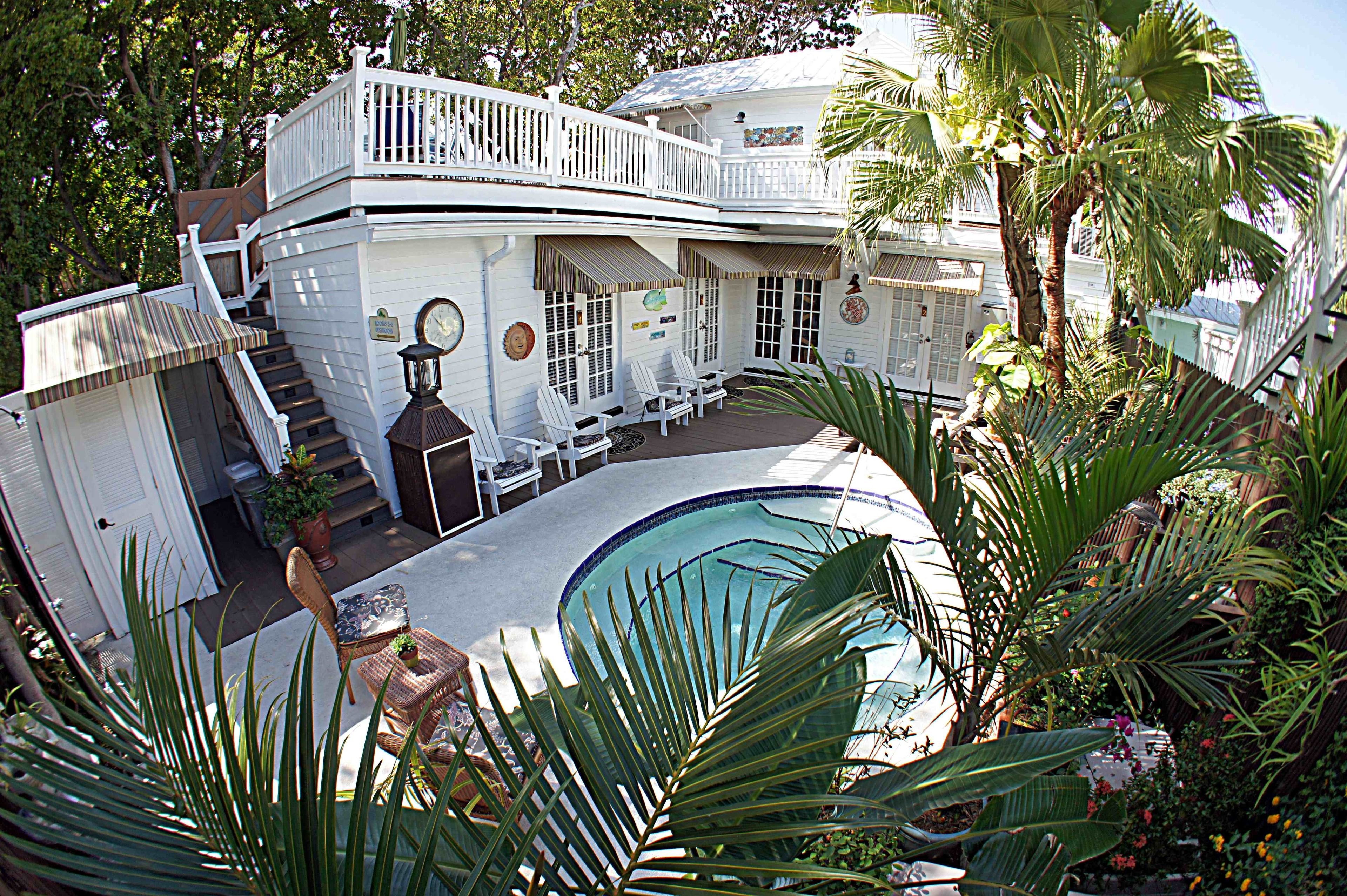 Una casa de dos pisos con piscina, mobiliario exterior y una escalera que lleva al nivel superior.