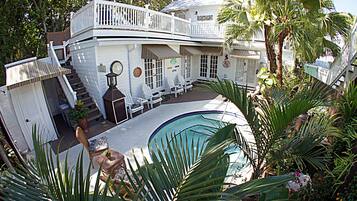 Una casa de dos pisos con piscina, mobiliario exterior y una escalera que lleva al nivel superior.