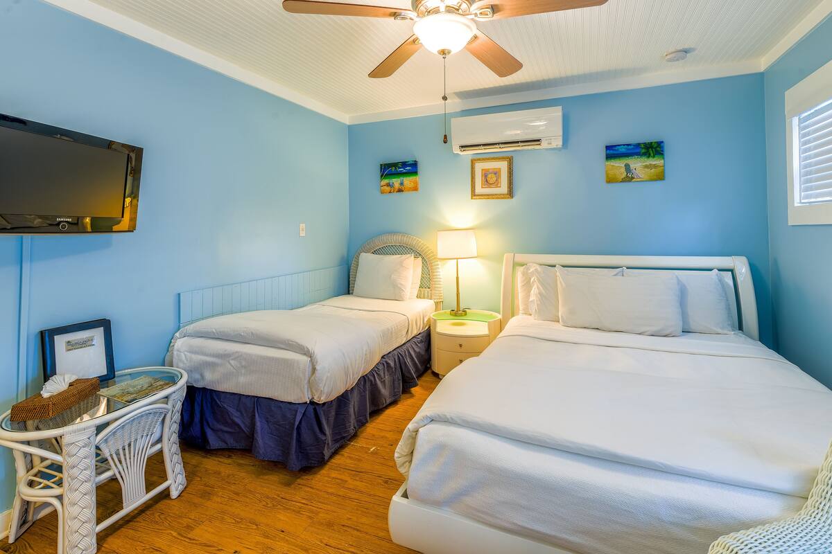 A room with two beds, a ceiling fan, a TV, and artwork on the walls.