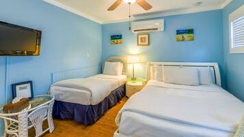 A room with two beds, a ceiling fan, a TV, and artwork on the walls.